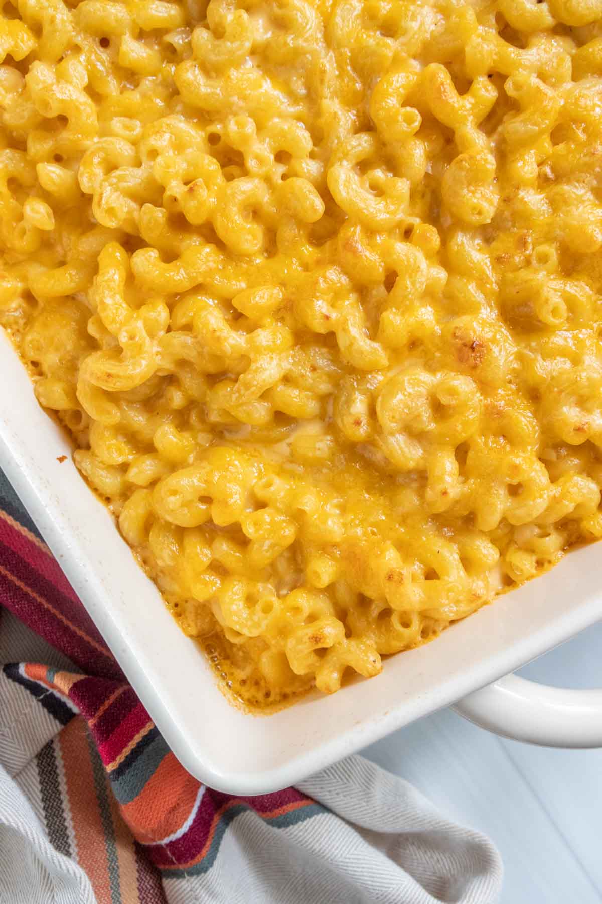 A baking dish filled with freshly baked mac and cheese with a golden, melted cheese topping. A striped cloth is partially visible beside the dish.