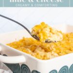 A spoon scoops creamy baked mac and cheese from a casserole dish with green patterns. Text above reads: "baked mac & cheese - creamy & comforting.