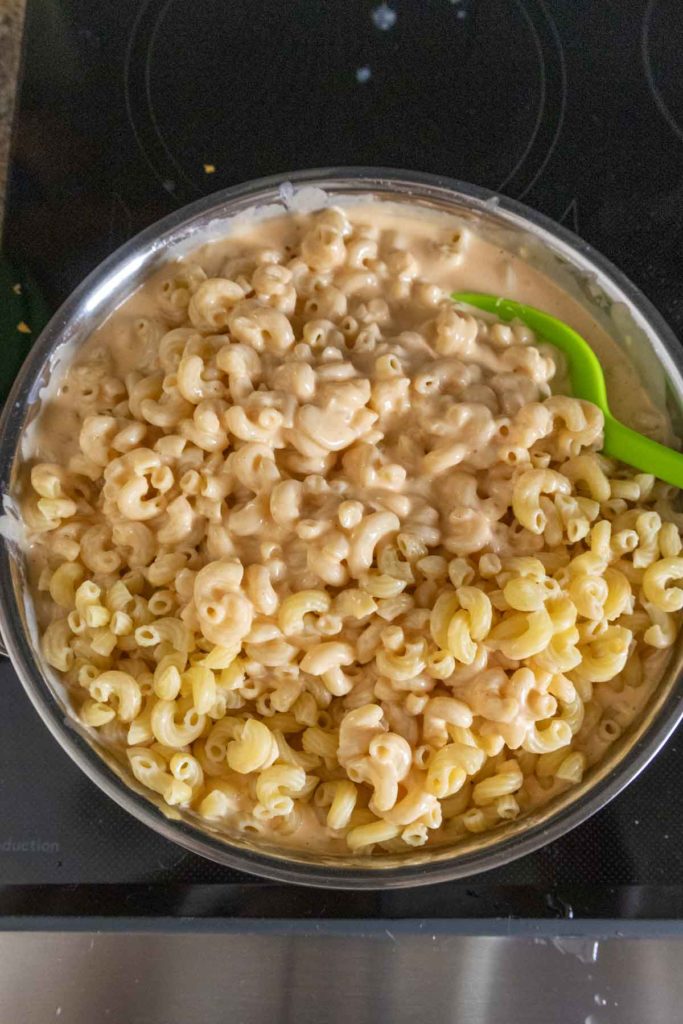 A bowl of creamy macaroni and cheese with a green spoon on a black stovetop.