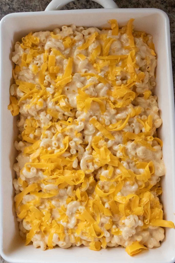 Baking dish filled with creamy macaroni and cheese topped with shredded cheddar.