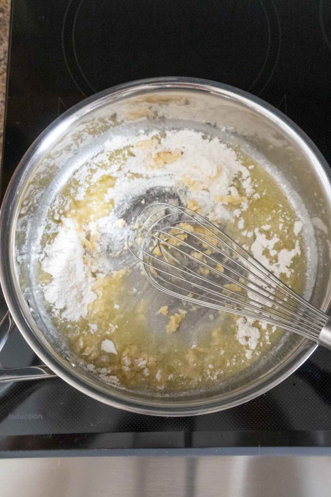 A whisk in a pan with melted butter and flour on an electric stove, beginning the process of making a roux.