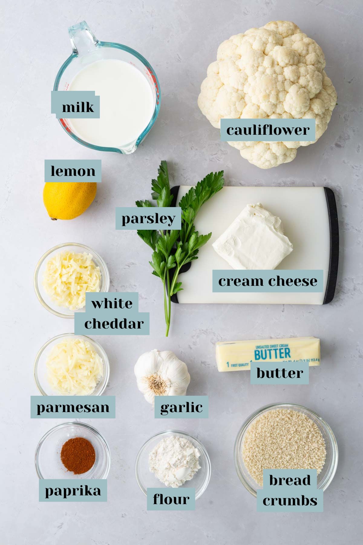 Ingredients displayed on a surface: cauliflower, milk, lemon, parsley, cream cheese, white cheddar, parmesan, garlic, flour, butter, bread crumbs, and paprika.