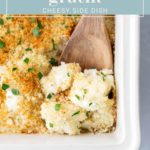 Cheesy cauliflower gratin topped with breadcrumbs in a white baking dish, with a wooden spoon scooping a portion.