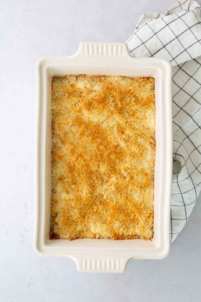 A rectangular baking dish with a golden-brown, crumb-topped casserole, placed next to a checkered cloth.