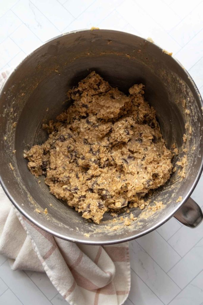 Cookie dough with chocolate chips in a metal mixing bowl, placed on a striped kitchen towel.