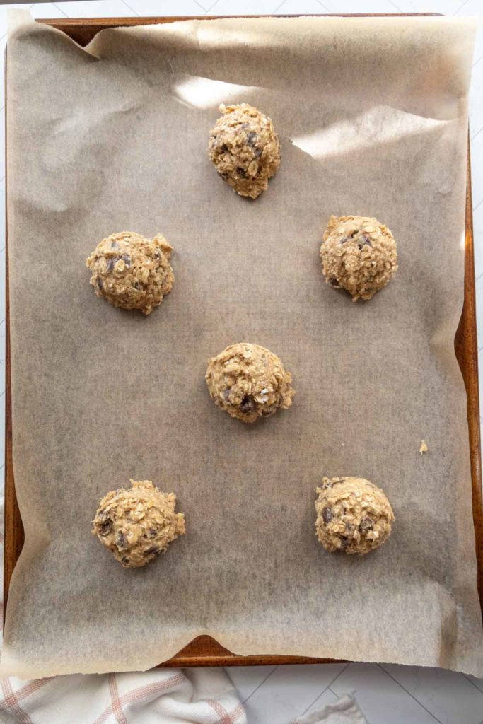 Six scoops of cookie dough on parchment paper lined baking sheet.