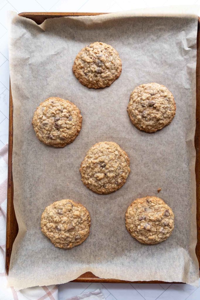 Six oatmeal cookies on a parchment-lined baking sheet.