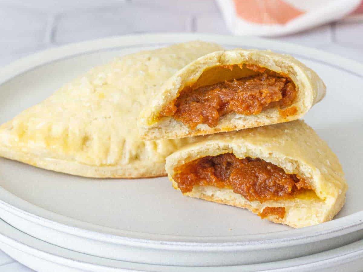 Pumpkin empanadas on a plate with one broken in half to see filling.