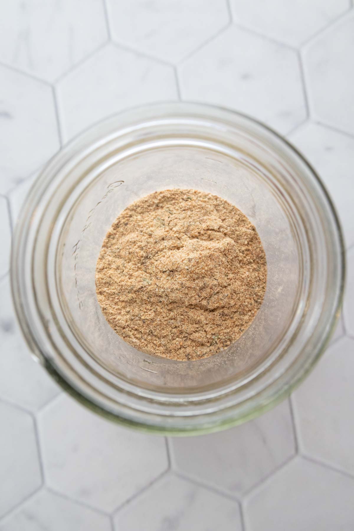 A glass jar filled with light brown powder on a hexagonal tiled surface.