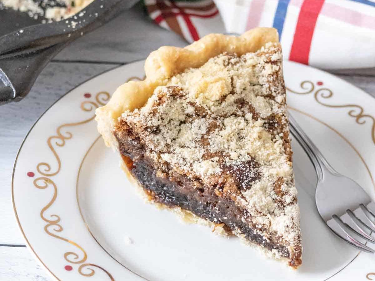 Slice of shoofly pie on a white plate with a fork beside.