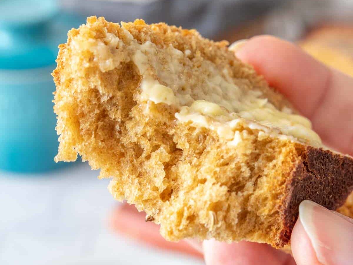 Torn slice of limpa bread with butter on it held close to camera to see interior texture.