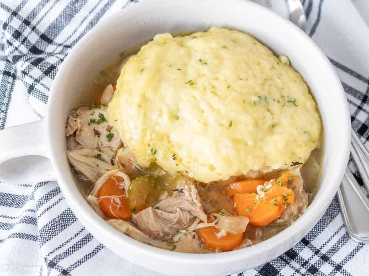 Two bowls filled with chicken and dumplings with spoons next to the bowls.