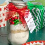 Mason jar with layered cookie mix ingredients, a red ribbon, and a tag.