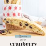 Cranberry pistachio biscotti in front of a white mug with red patterns, placed on a light surface.