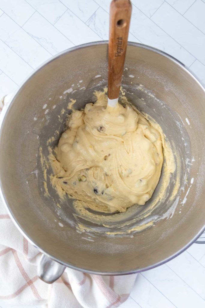 Bowl of cookie dough with chocolate chips and a wooden spatula on a white tiled surface.