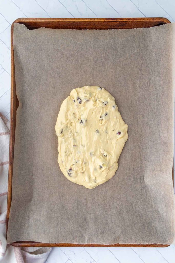 Cookie dough with visible chocolate chips spread on parchment paper on a baking sheet.