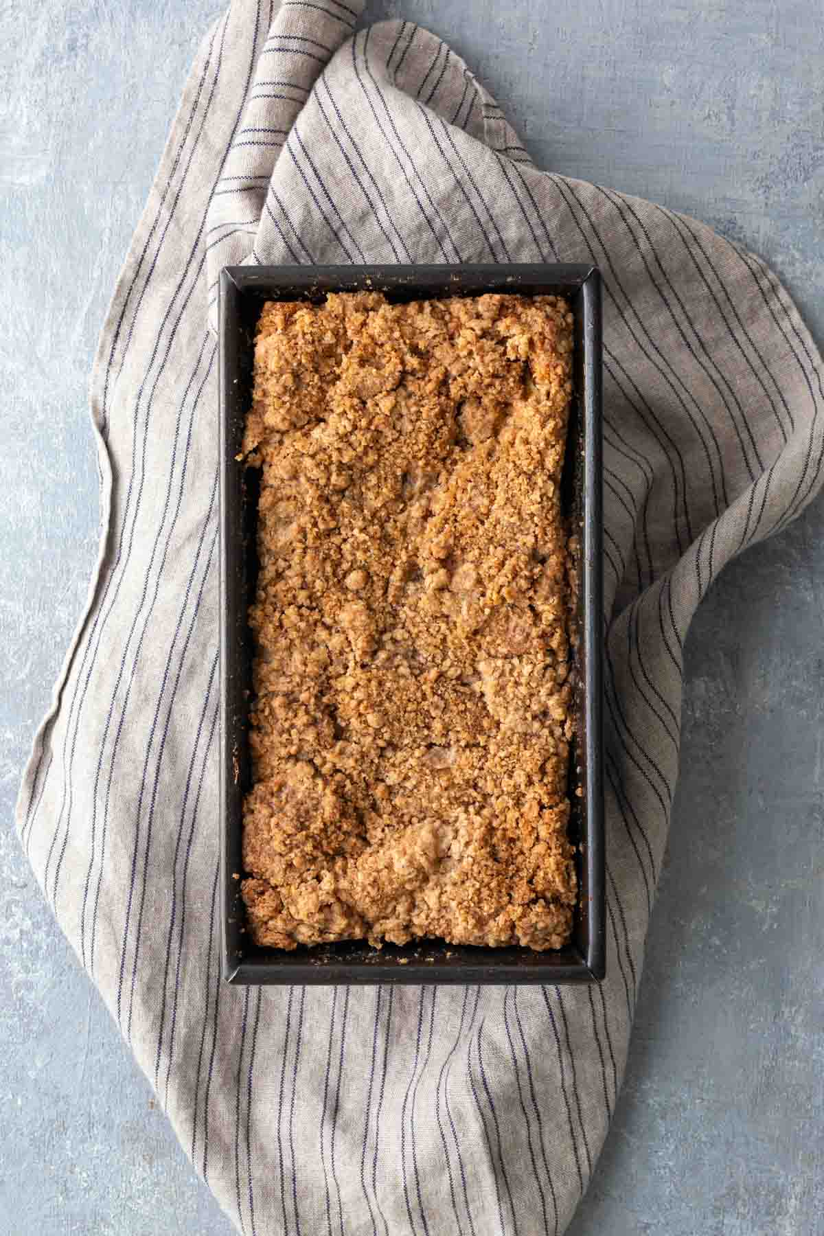 Loaf pan with crumb-topped cake on a striped cloth.