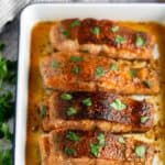 Four seasoned and cooked salmon fillets garnished with parsley in a baking dish.