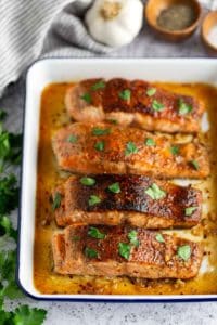 Four seasoned and cooked salmon fillets garnished with parsley in a baking dish.