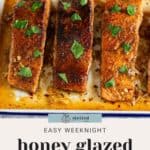 Close-up of three honey-glazed salmon fillets with herbs on top in a baking dish. Text reads, "Easy Weeknight Honey Glazed Salmon.