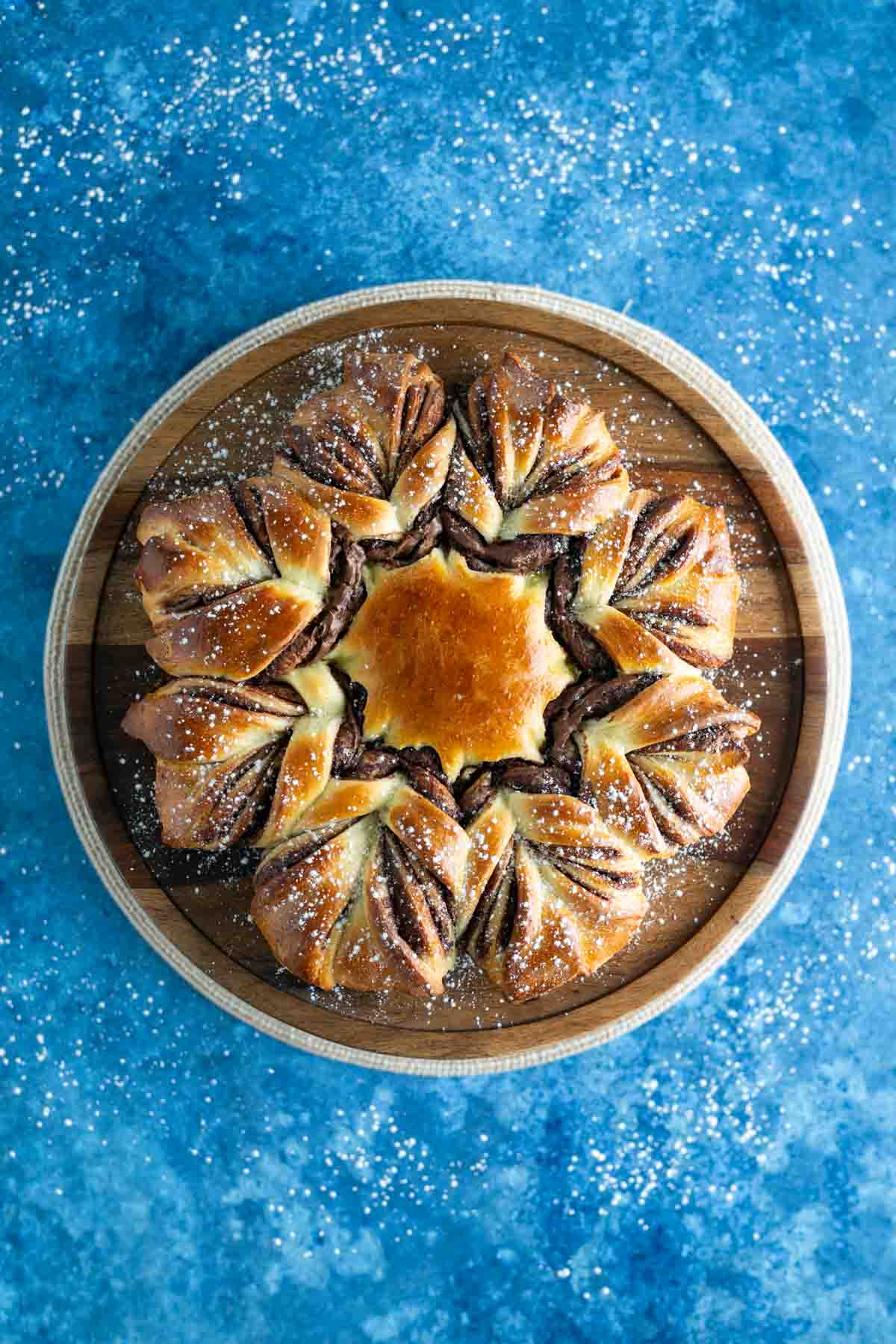 Star-shaped pastry dusted with powdered sugar on a wooden plate against a blue background.