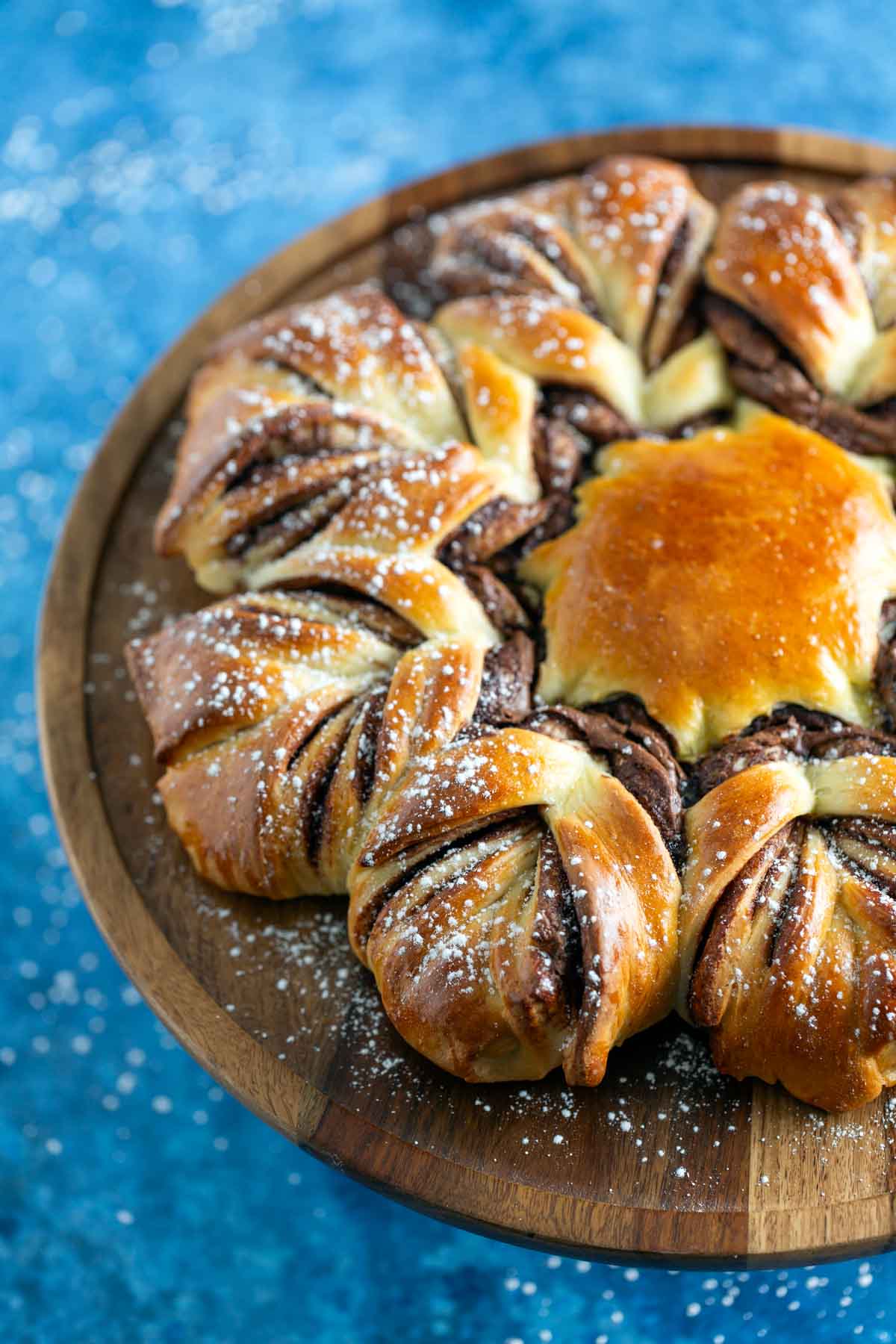 A star-shaped chocolate bread on a wooden platter, dusted with powdered sugar, set against a blue surface.