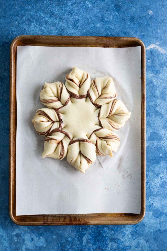 A star-shaped, unbaked pastry with twisted layers of dough and chocolate filling on a parchment-lined baking sheet.