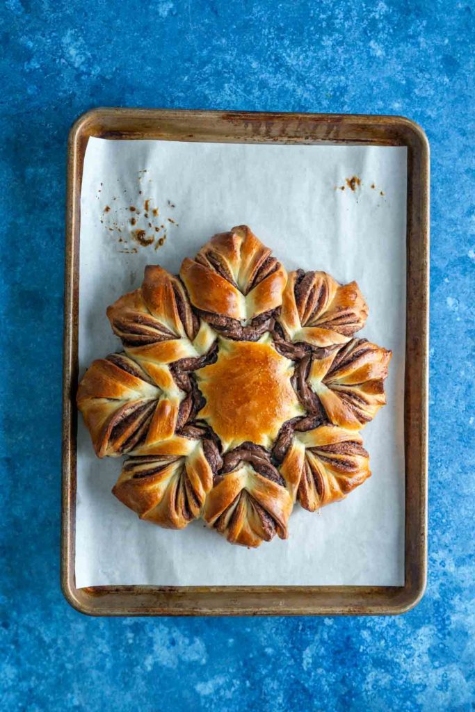 Star-shaped bread with swirled chocolate filling on a parchment-lined baking sheet against a blue background.