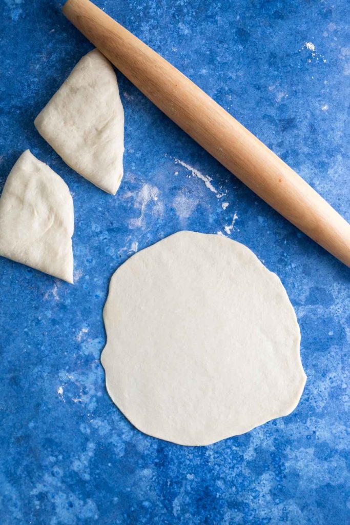 Rolling pin and rolled out dough with two dough pieces on a blue surface.