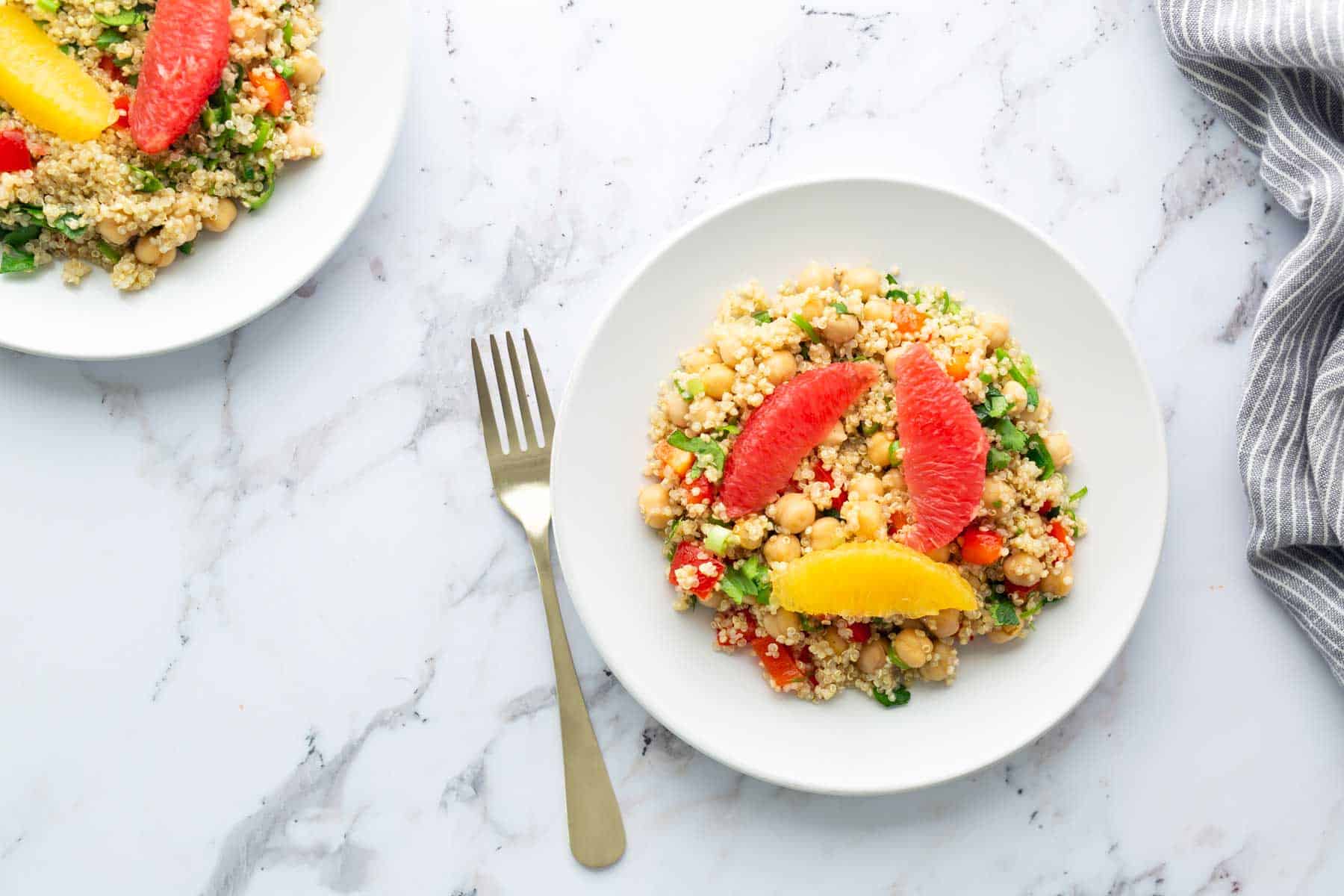 Two plates of quinoa salad on a marble table with a fork.