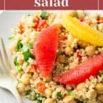 A colorful citrus quinoa salad with grapefruit, orange slices, chickpeas, and chopped greens on a white plate with a fork.