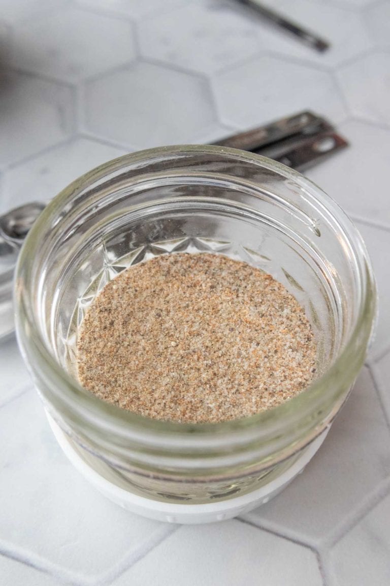 A small glass jar filled with a light brown, finely ground powder sits on a hexagonal tile surface.