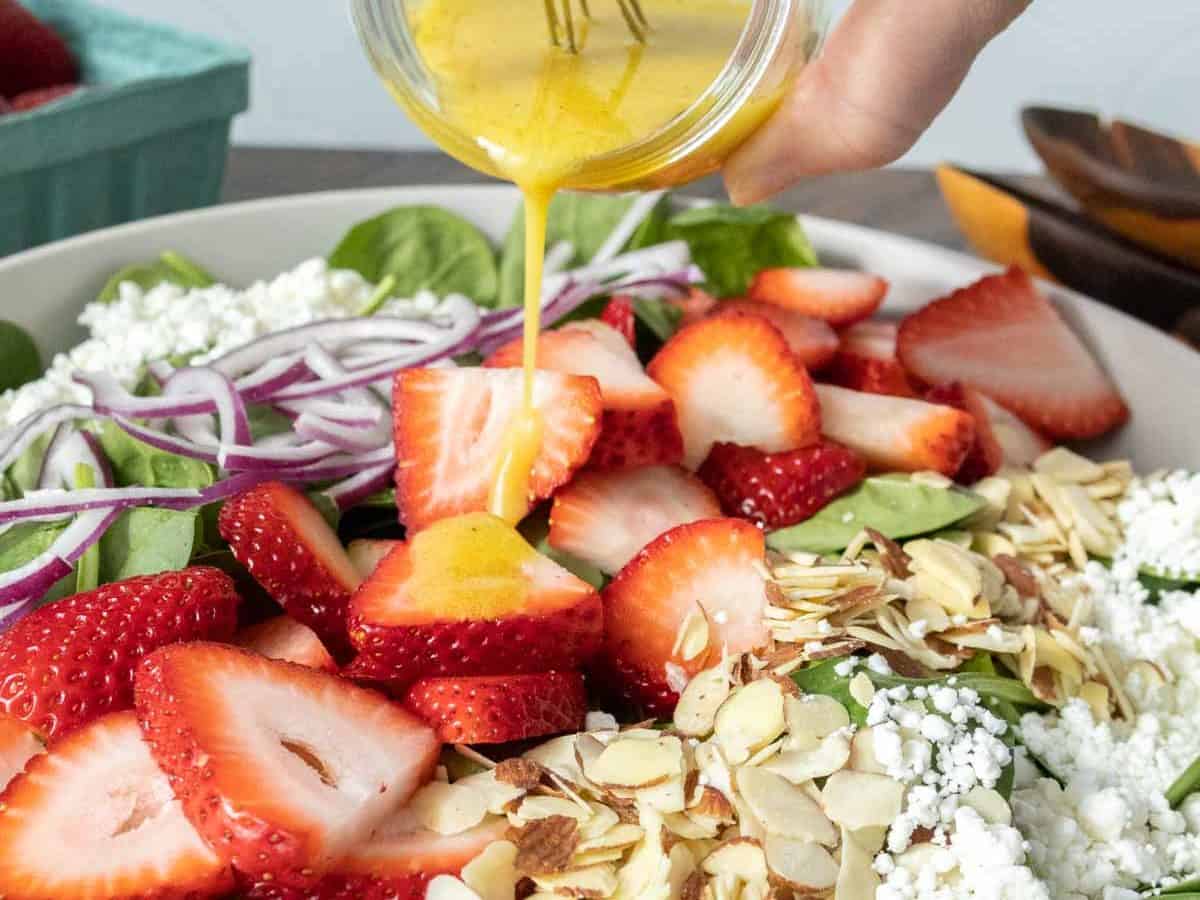 Pouring dressing onto strawberry spinach salad.