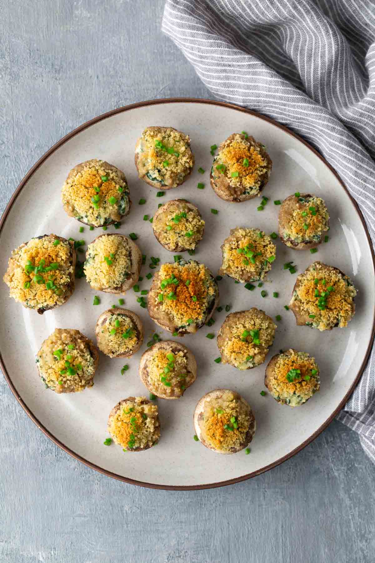 A plate of stuffed mushrooms topped with breadcrumbs and herbs. A striped cloth is placed beside the plate.