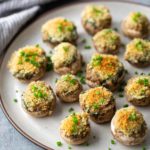 Plate of stuffed mushrooms topped with breadcrumbs and chopped chives on a textured gray surface.