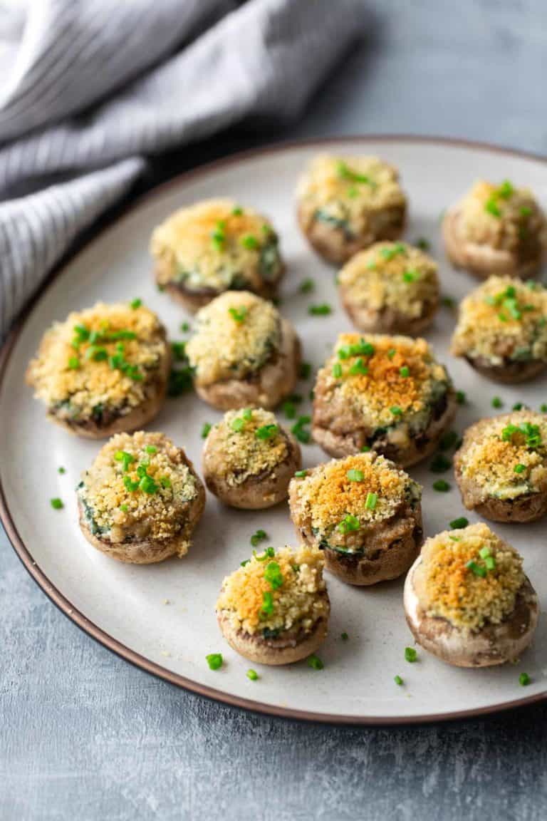 Plate of stuffed mushrooms topped with breadcrumbs and chopped chives on a textured gray surface.