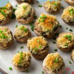 A plate of stuffed mushrooms topped with breadcrumbs and chopped chives, arranged neatly.