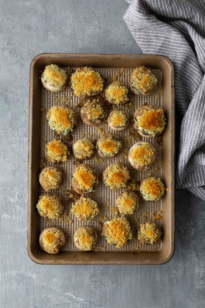 Baking tray with stuffed mushrooms topped with breadcrumbs, next to a striped cloth.