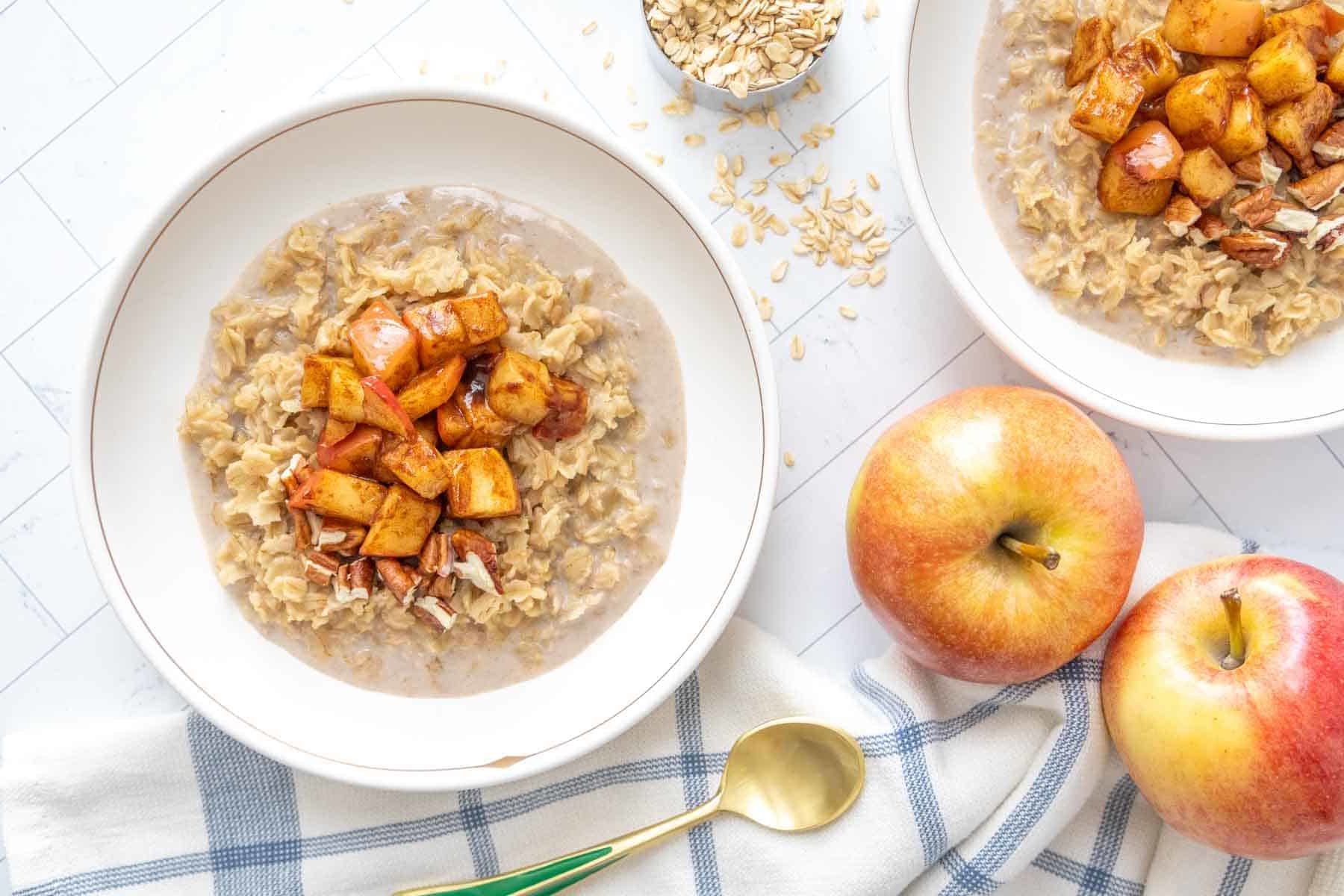 Two bowls of oatmeal with apples and oats.