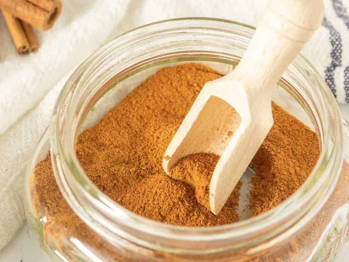 Apple pie spice in a glass bowl with cinnamon sticks.