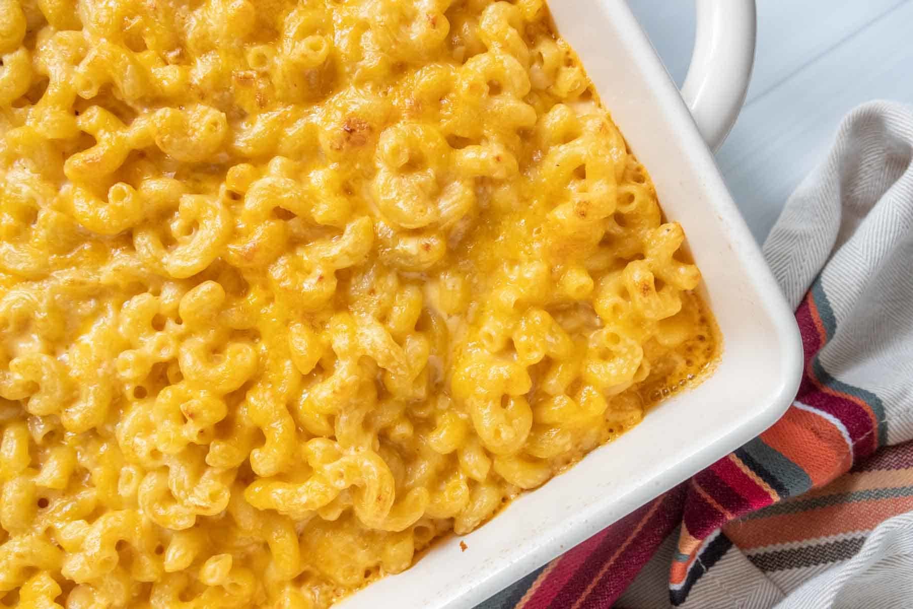 A baking dish filled with freshly baked mac and cheese with a golden, melted cheese topping. A striped cloth is partially visible beside the dish.