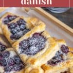 Pastries topped with blueberries and sprinkled with powdered sugar on a wooden tray.