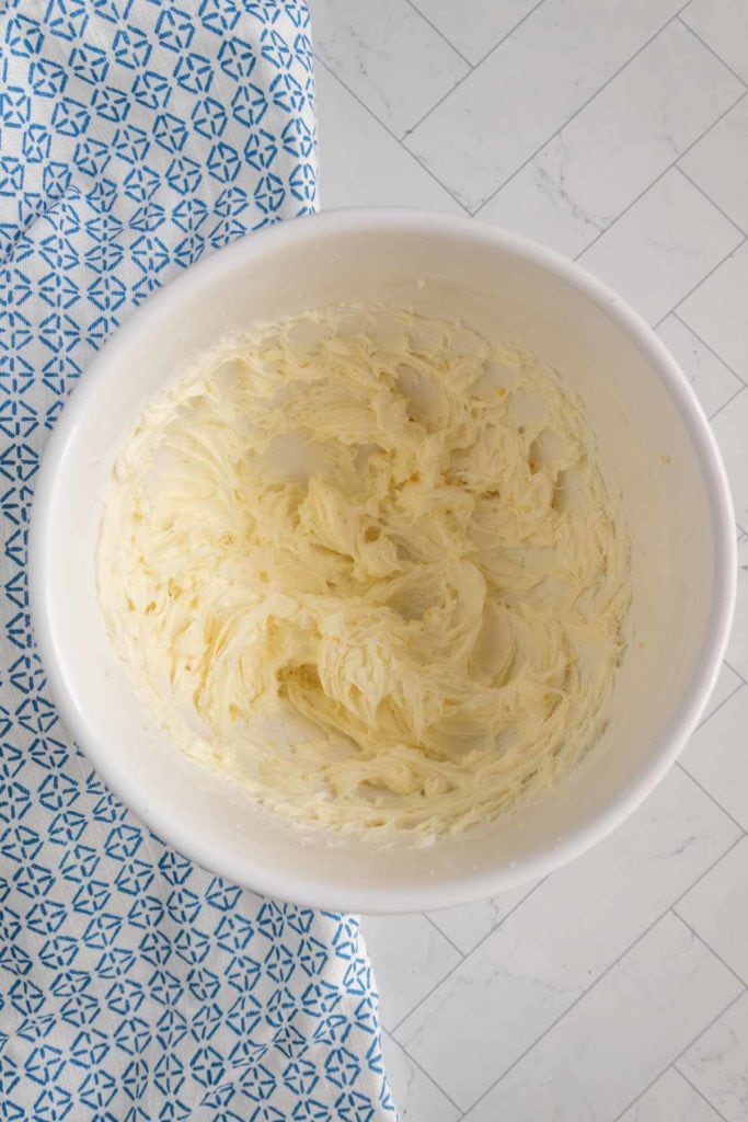 A white bowl filled with whipped, creamy butter on a tiled surface next to a blue patterned cloth.