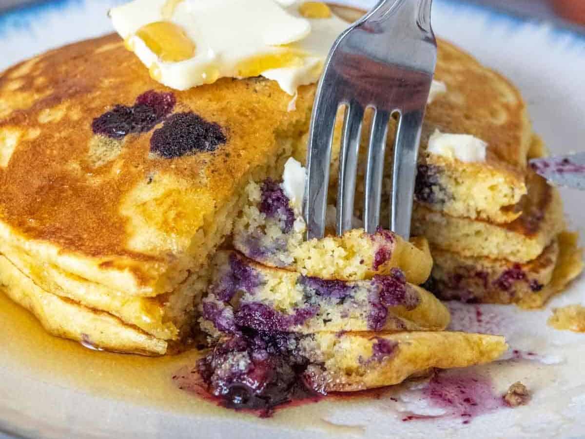 Fork piercing cut pieces of blueberry pancakes.