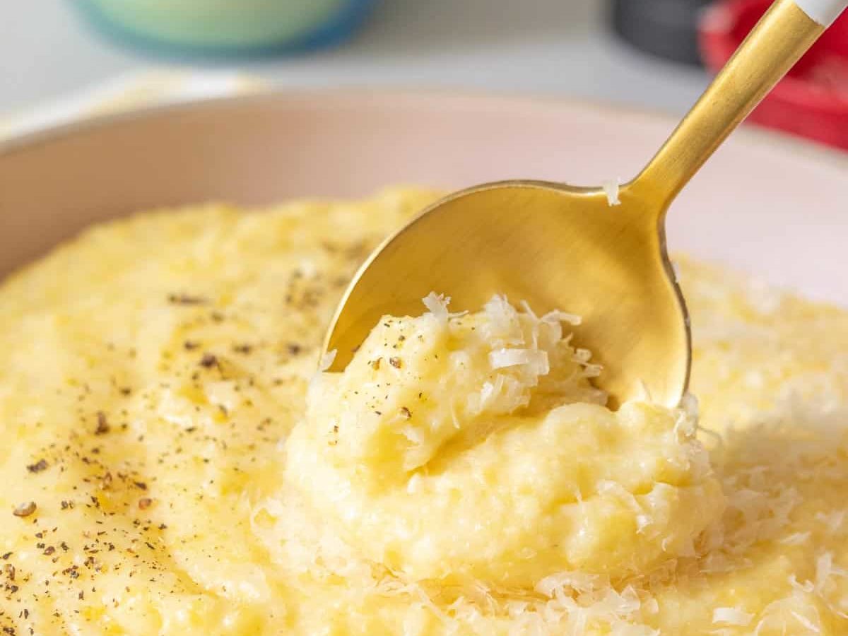 Bowl of cheesy polenta with a spoon stirring.