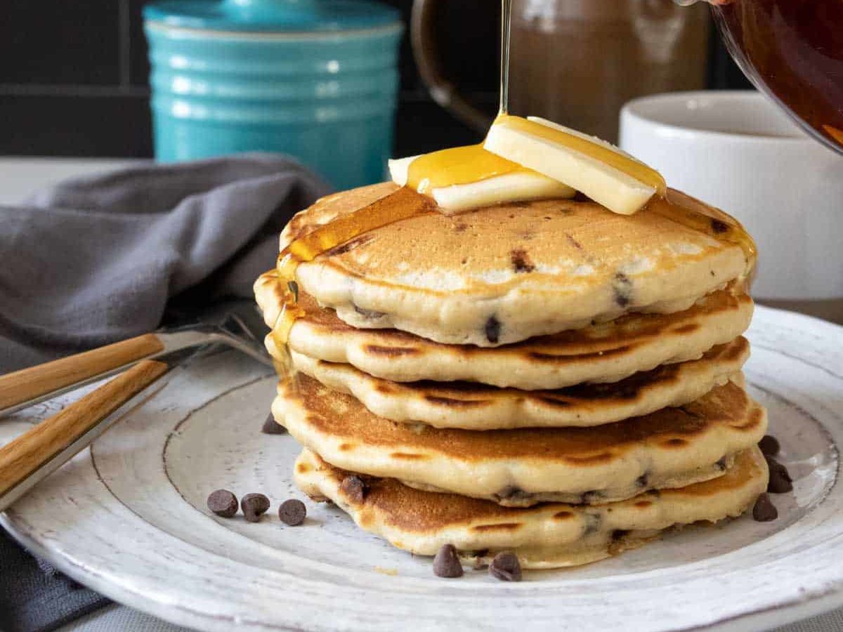 Maple syrup being poured on top of chocolate chip pancakes.