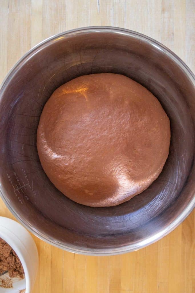 A ball of chocolate dough in a metal mixing bowl on a wooden surface.