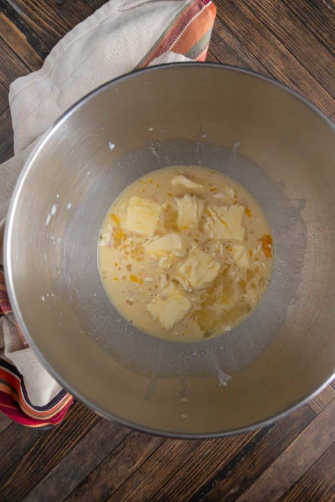 Mixing bowl containing butter, eggs, and flour on a wooden surface with a striped cloth nearby.