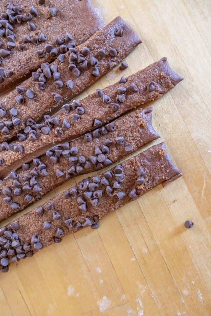 Five chocolate-coated pastry sticks with chocolate chips on a wooden surface.