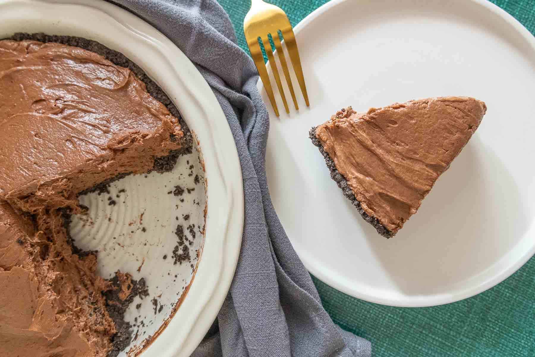 Slice of chocolate peanut butter pie on a plate with rest of pie nearby.